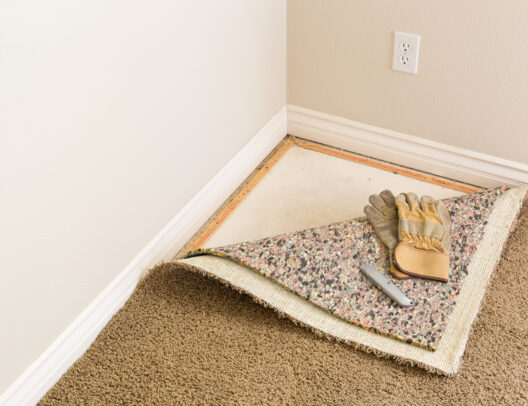 Construction Gloves and Utility Knife On Pulled Back Carpet and Pad In Room.
