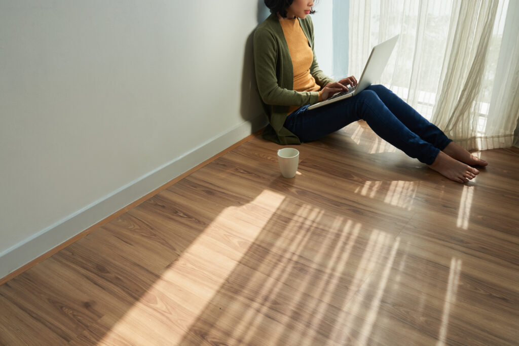Cropped image of female student sitting on the floor in her room and working on laptop